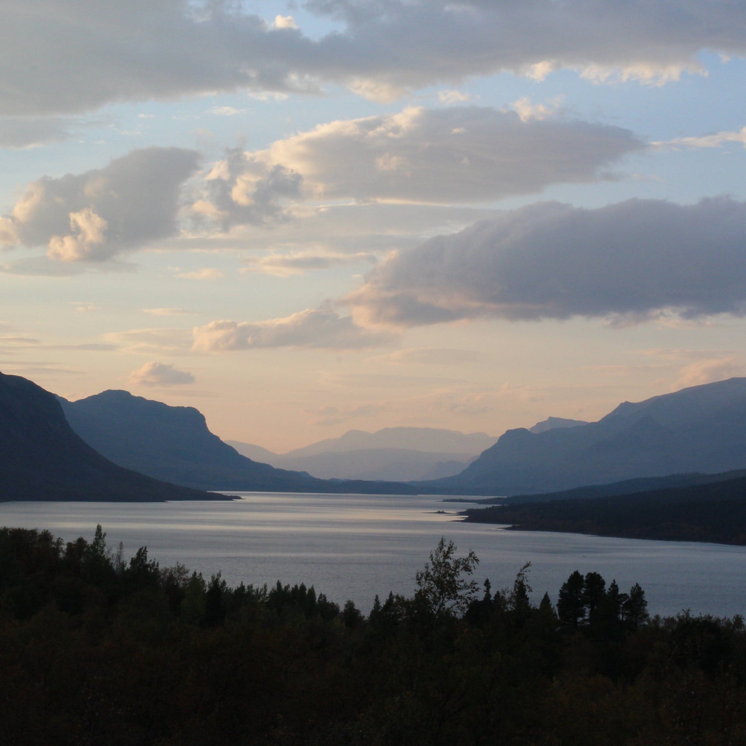 Scenic view of a lake surrounded by mountains with a cloudy sky.